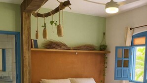 Een slaapkamer met een bed, nachtkastje, kaptafel, plafondventilator en een raam met blauwe luiken.