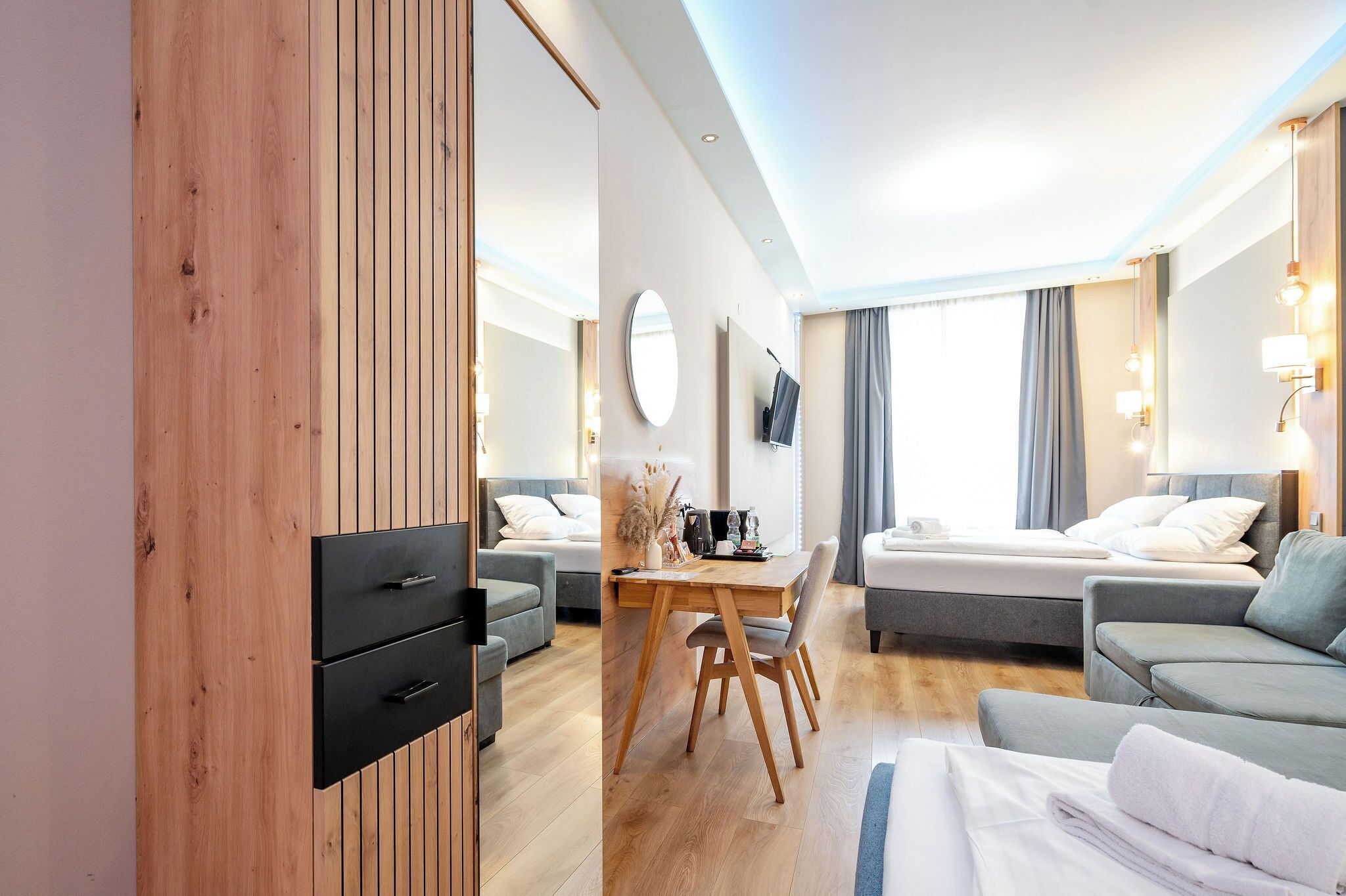 Una habitación de hotel moderna con un armario de madera, una mesa de comedor, dos sofás, una cama y un televisor.