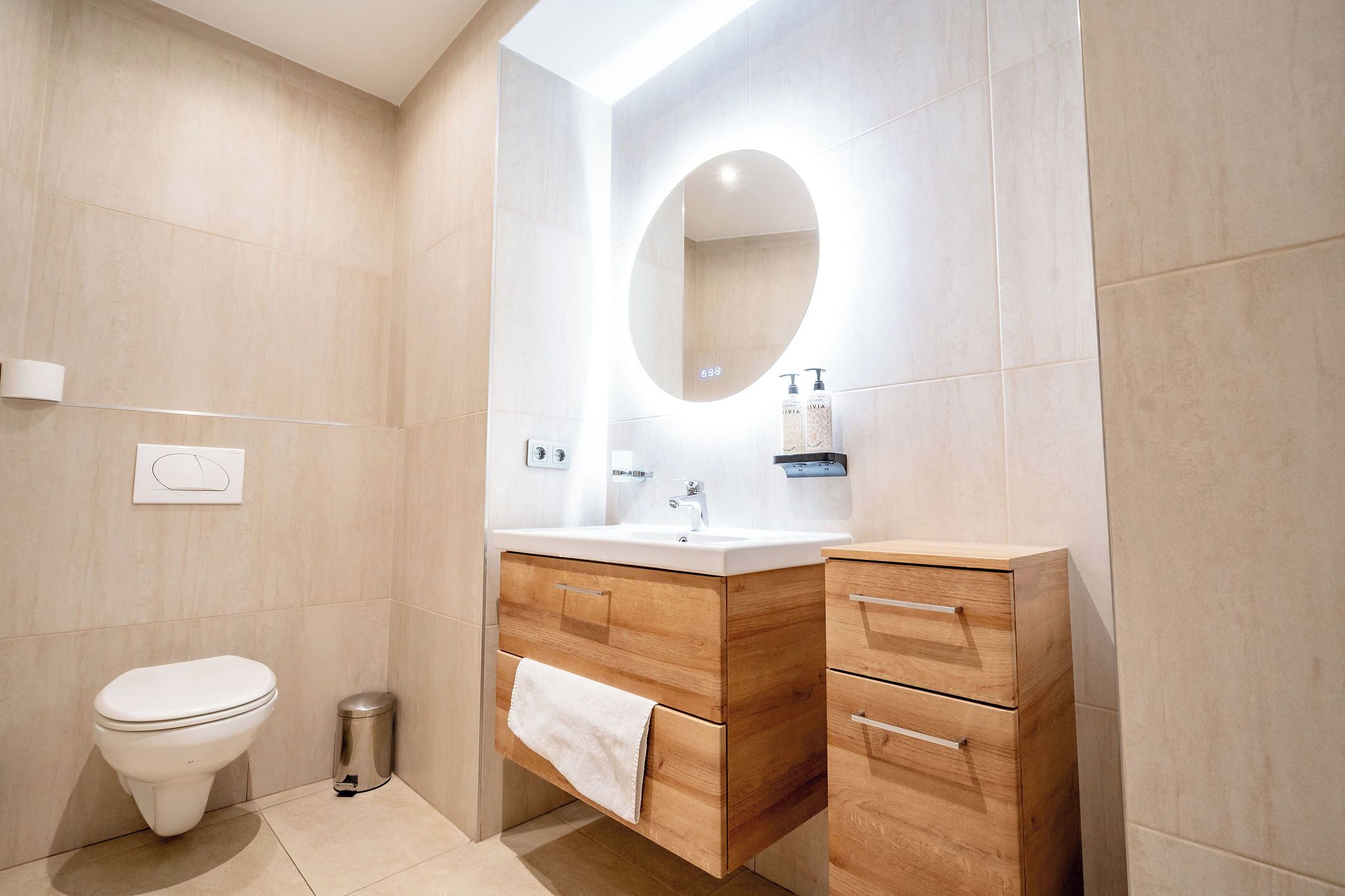 Un baño moderno con inodoro, tocador con espejo y un cubo de basura.