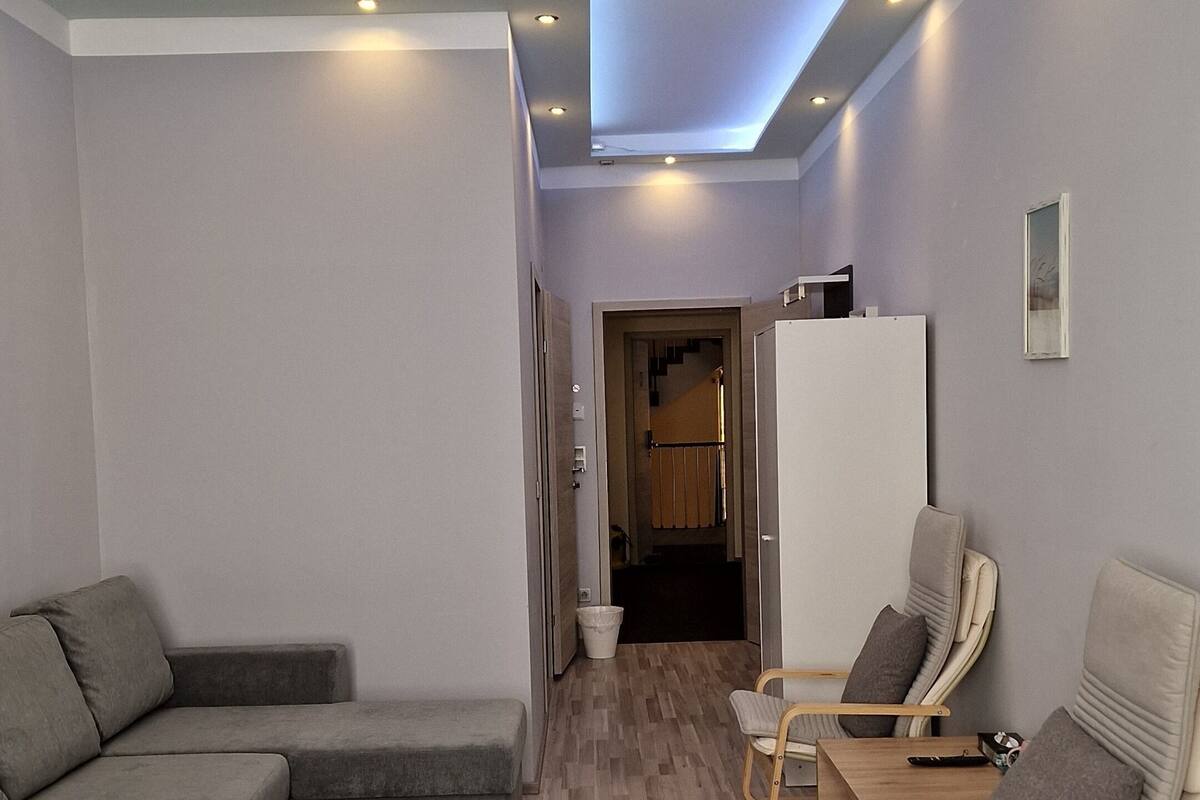 Een moderne hotelkamer met een bank, twee fauteuils, een bed en een gang die leidt naar een trap.