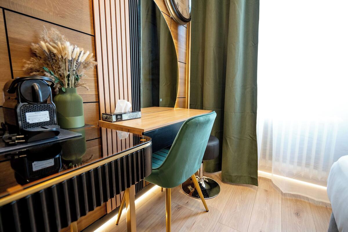Een moderne hotelkamer met een houten bureau, een groene stoel, een radiator en een klok aan de muur.