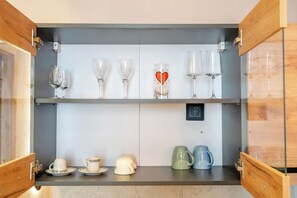 A kitchen with two shelves, one holding wine glasses and the other holding cups and a coffee maker. - Elegance Studios Wien (Vienna)