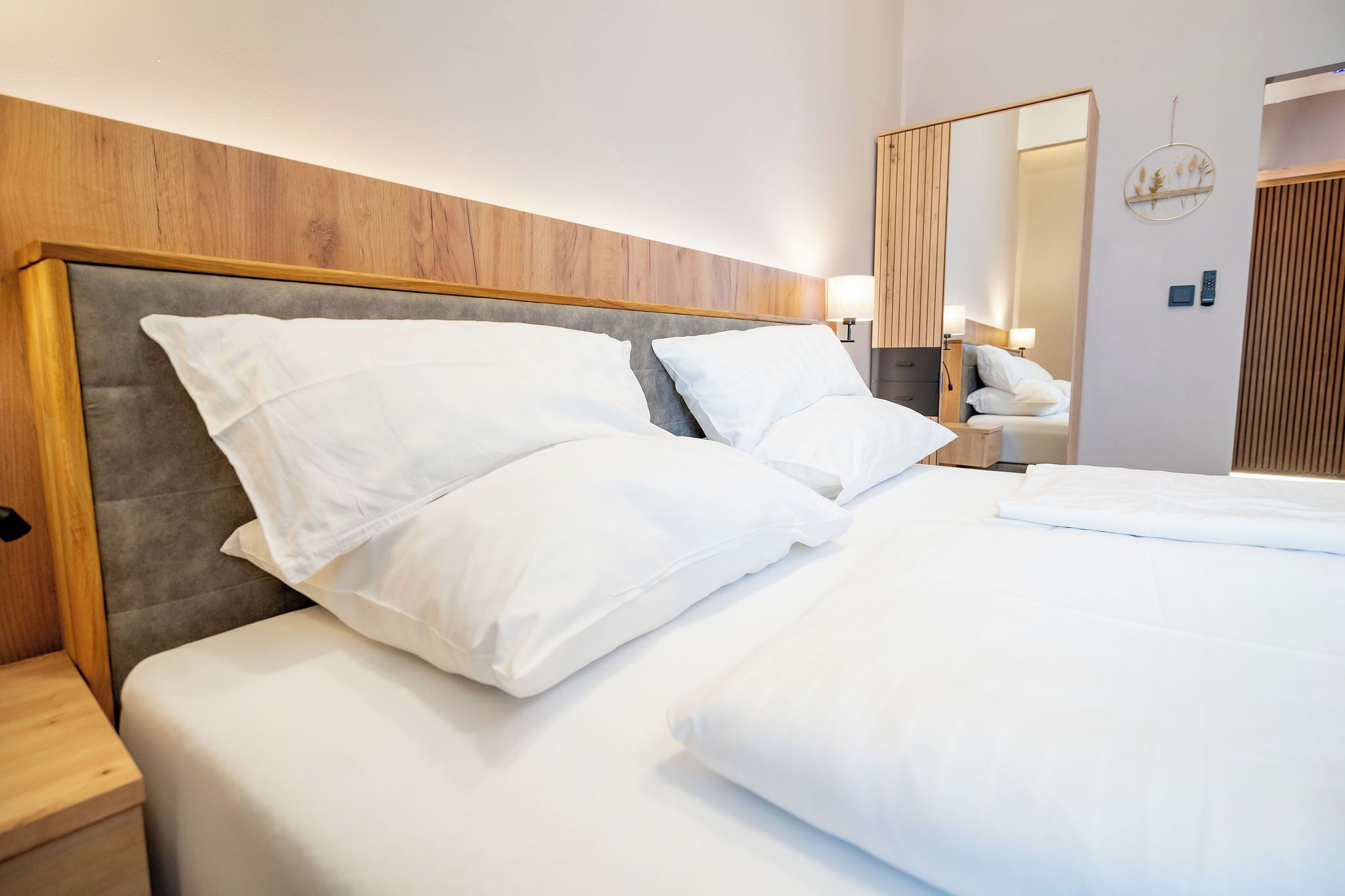 A neatly made bed with white linens, a wooden headboard, and a nightstand with a lamp.