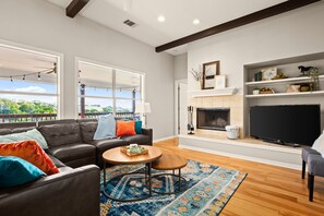 A living room with a fireplace, a television, and a large window overlooking a balcony. - Relaxing Getaway w/ Lake Travis Views + Hot Tub (Leander)