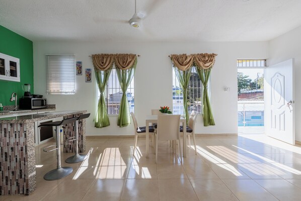 A bright kitchen with a green wall, a bar area, and a dining table with chairs.