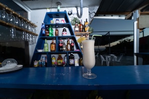 A bar area with a blue counter, a glass of a white beverage, and shelves stocked with various bottles.