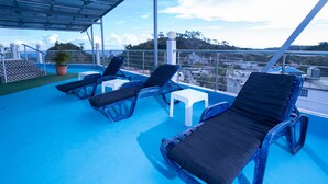 Eine Dachterrasse mit blauem Boden, weißen Tischen und schwarzen Loungesesseln.