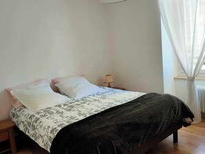 A bedroom with a bed, two pillows, a bedside lamp, and a window with curtains.