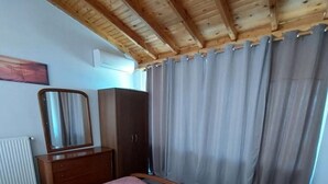 Un dormitorio con techo de madera, una cama con colcha rosa, un aparador, un espejo y una ventana con cortinas.