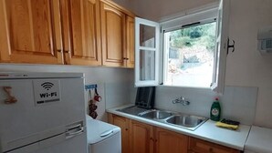 Cocina compacta con armarios de madera, un refrigerador blanco, horno integrado y ventana con vistas al exterior.
