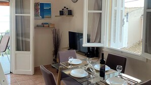 Un comedor con una mesa de vidrio, cuatro sillas, un televisor y un reloj en la pared.