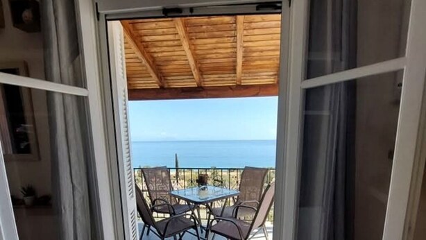 Puerta abierta que da a un patio con mesa y sillas, con vista a un cuerpo de agua.