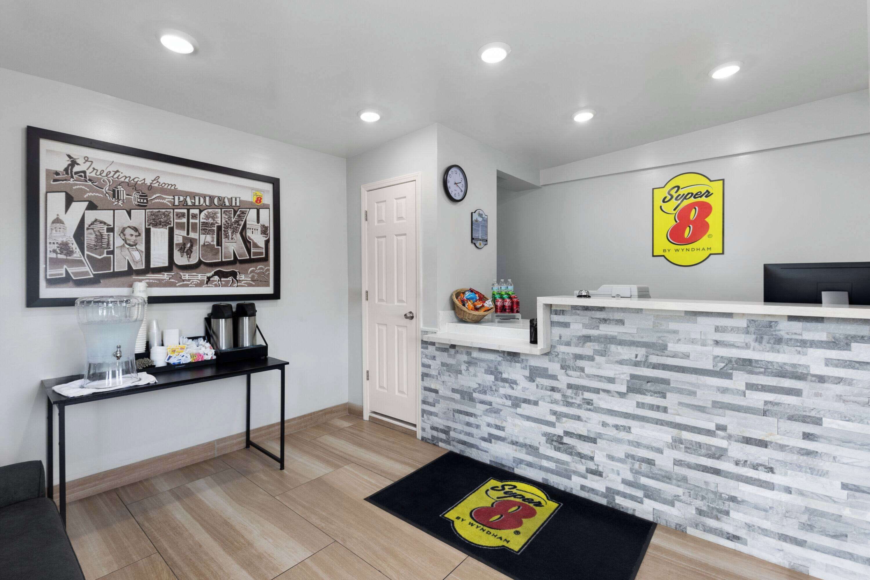 A reception area with a Kentucky-themed wall art, a Super 8 logo, a coffee station, and a clock.