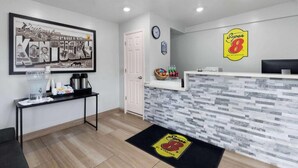 A reception area with a framed welcome sign, a clock, a water dispenser, and a Super 8 logo on the wall.