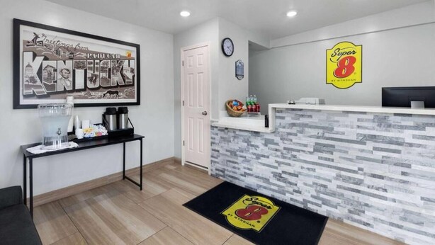 A reception area with a framed welcome sign, a clock, a water dispenser, and a Super 8 logo on the wall.