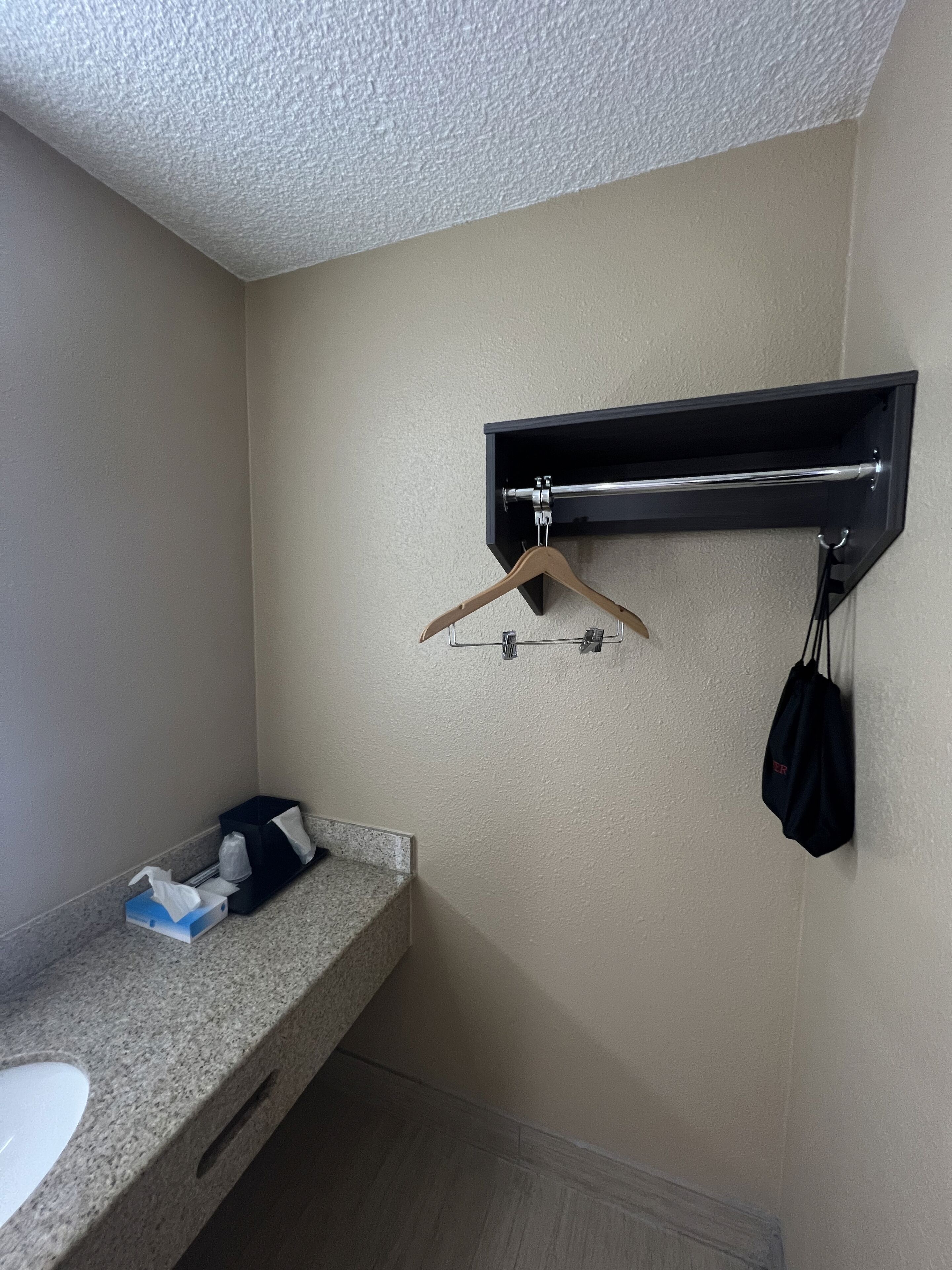 Un baño con encimera de granito, un perchero, una toalla negra y un bolso negro colgado en la pared.