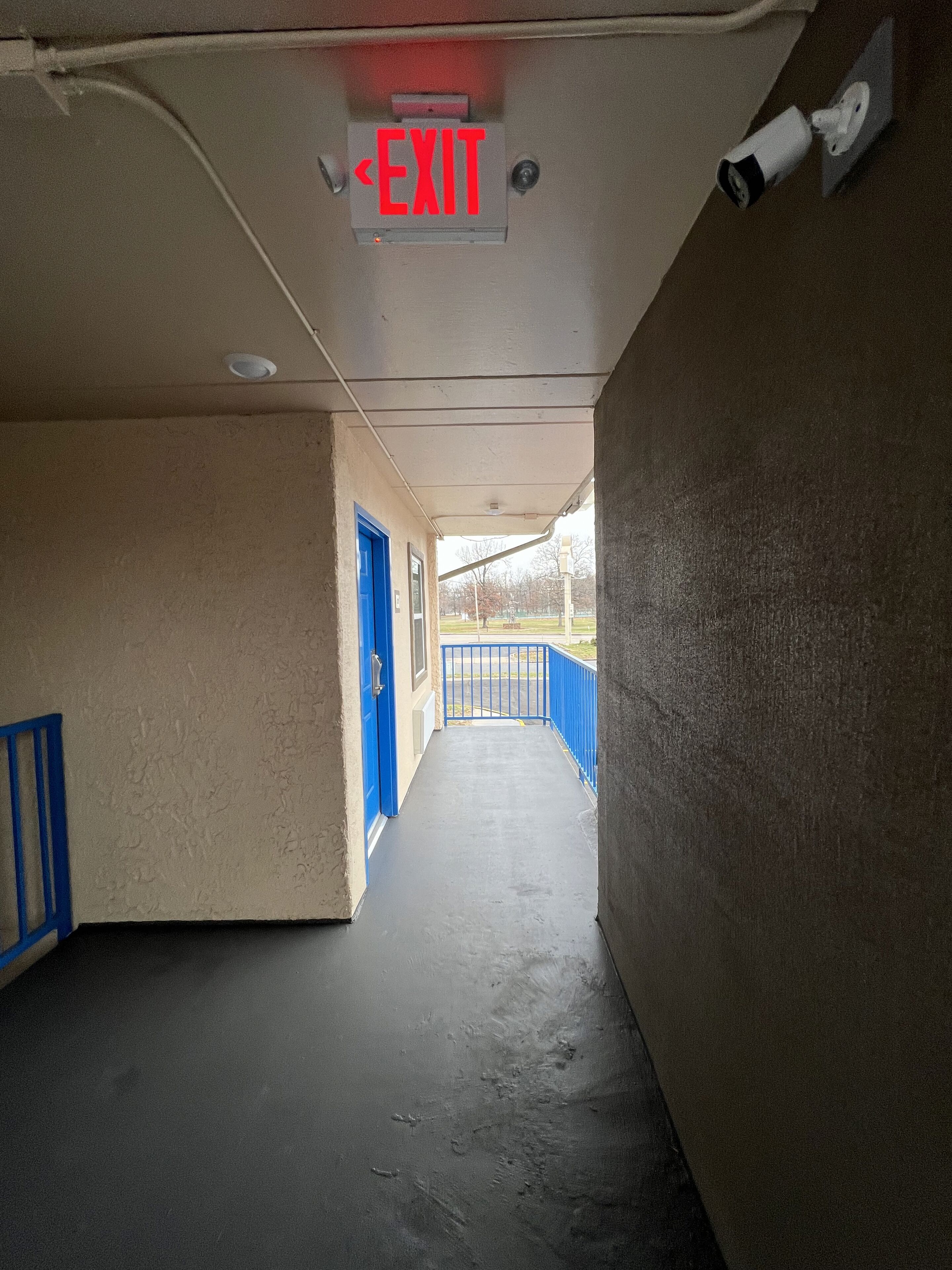 A corridor with an exit sign, blue doors, and a concrete floor.