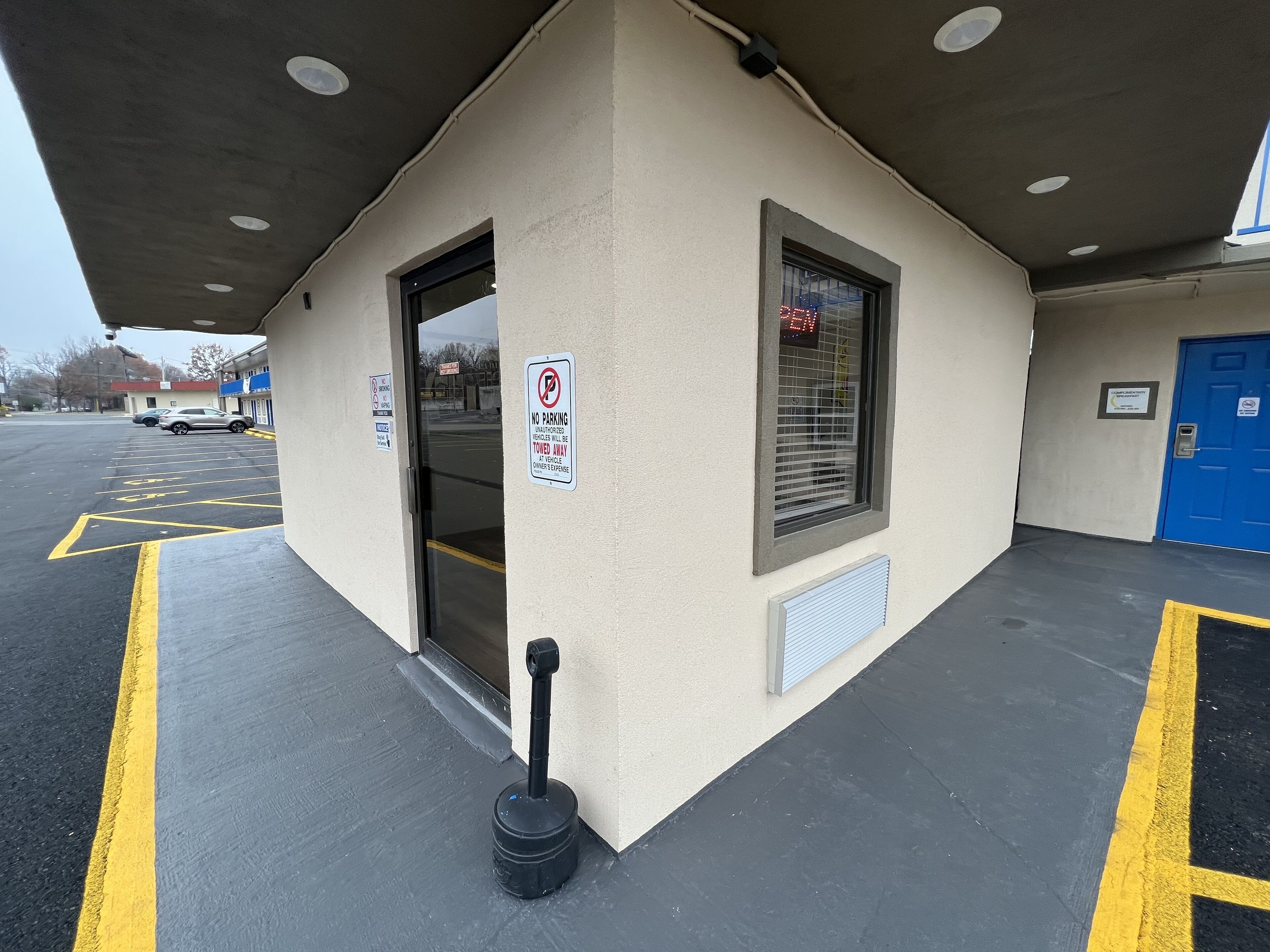 A parking area with marked spaces, a no parking sign, and a building entrance with a blue door.