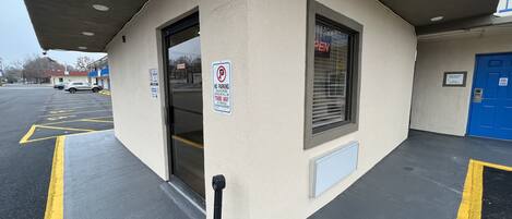 A parking area with marked spaces, a no parking sign, and a building entrance with a blue door.