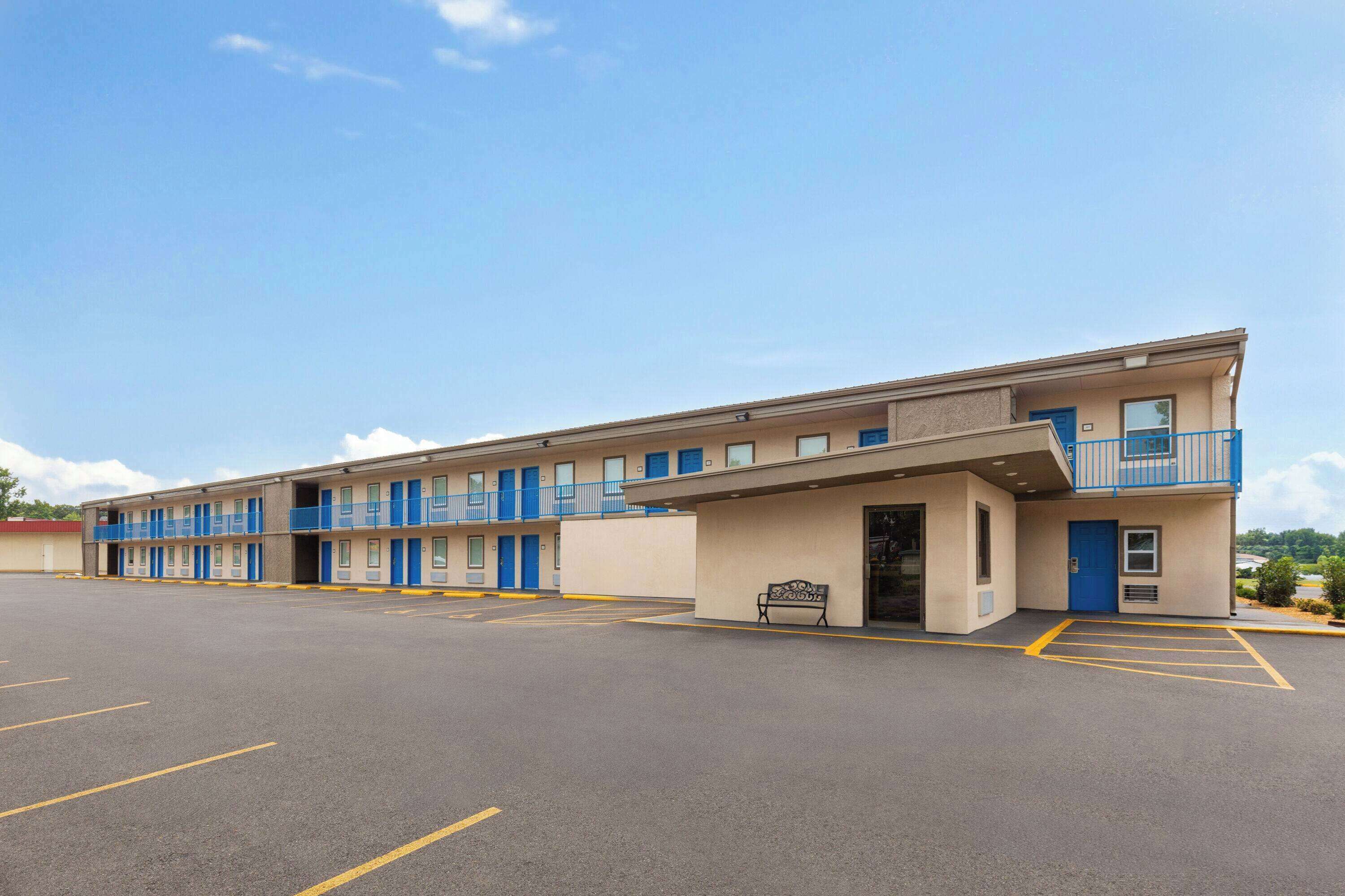 A motel with a row of rooms, a parking lot, and a bench outside.