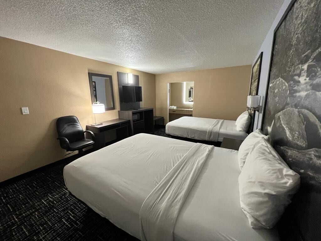 A hotel room with two beds, a desk, a chair, and a television.