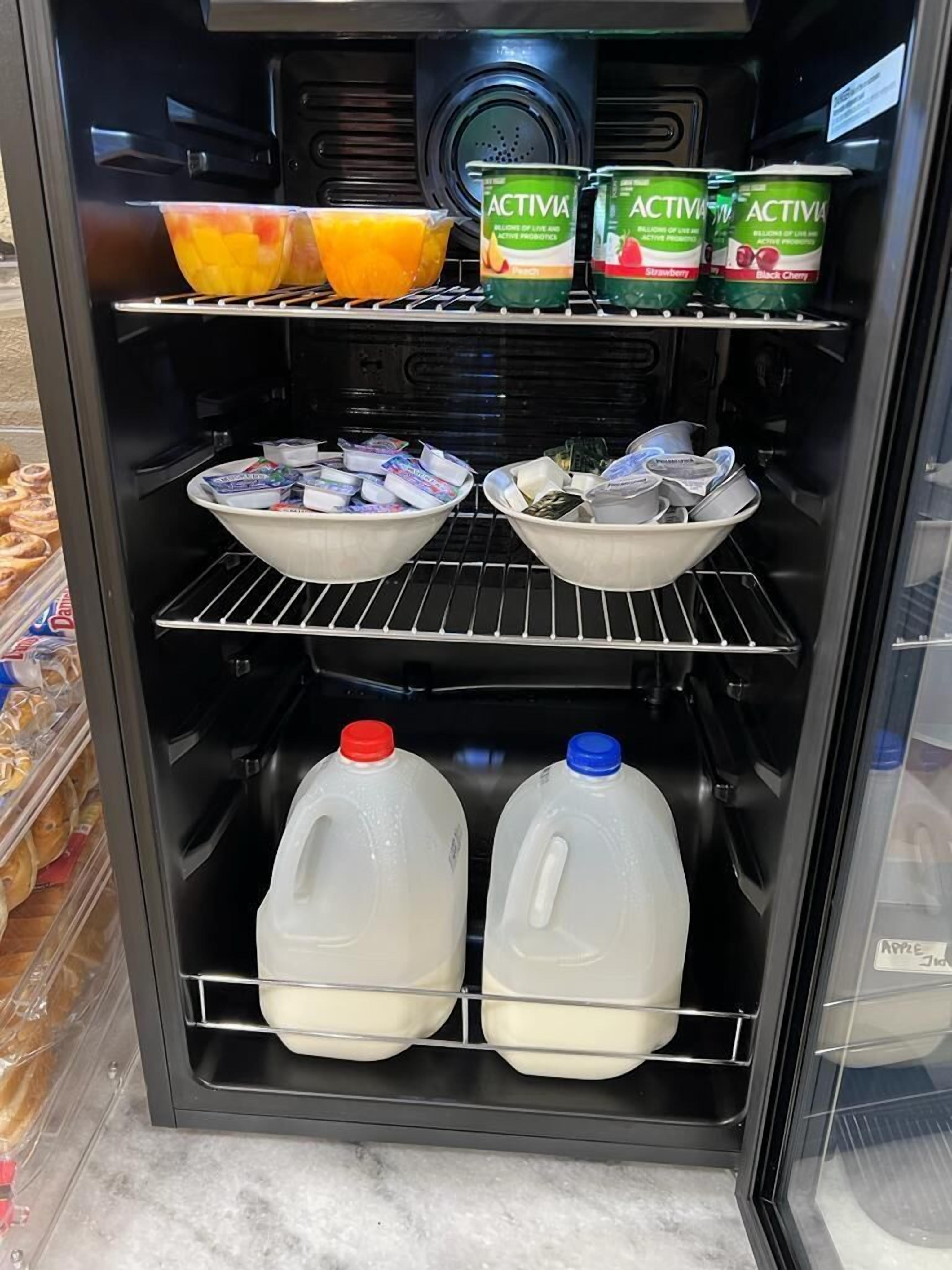 A refrigerated display case with various food items including yogurt, milk, and fruits.