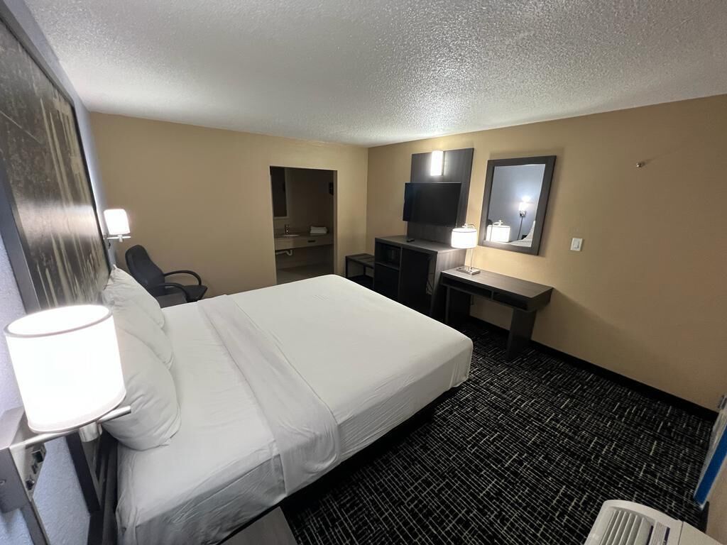 Une chambre d’hôtel avec un lit, un bureau, une télévision et un miroir.