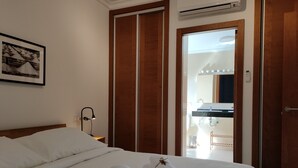A hotel room with a neatly made bed, a bedside lamp, a framed picture on the wall, and a door leading to a bathroom with a mirror and sink. - Villa Rosa (Playa Blanca)