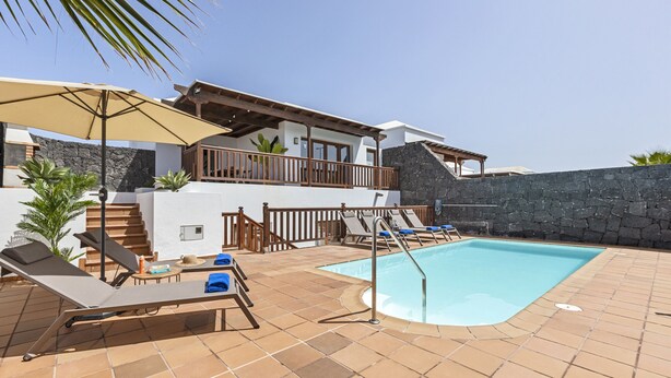 A pool area with lounge chairs, a wooden deck, and a stone wall. - Villa Rosa (Playa Blanca)