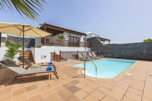 Un espace piscine avec des chaises longues, une terrasse en bois et un mur en pierre.