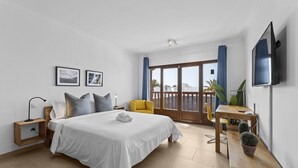 A modern hotel room with a large bed, a desk, a chair, and a balcony with a view. - Villa Rosa (Playa Blanca)