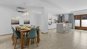 A modern kitchen with white cabinets, a central island, and a dining area with a wooden table and chairs. - Villa Rosa (Playa Blanca)