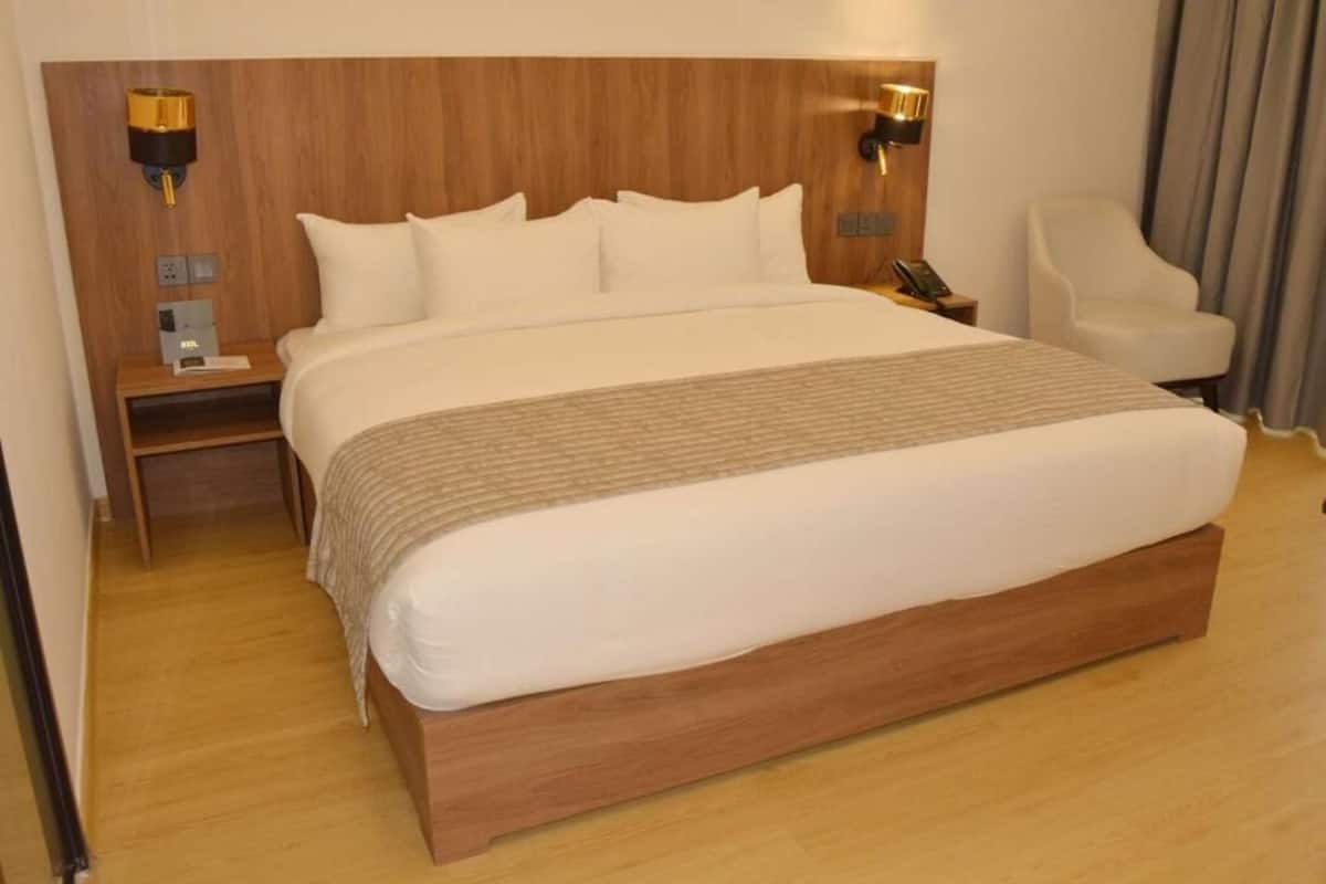 Una habitación de hotel con una cama grande, cabecera de madera, lámparas de noche, una silla y una mesita de noche.