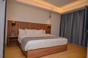 A neatly made bed with a wooden headboard, two bedside tables with lamps, and a large window with curtains.