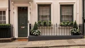 Une maison de ville traditionnelle avec une porte verte, deux fenêtres avec volets et une clôture en métal noir agrémentée de jardinières.
