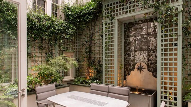 Une terrasse extérieure avec une table et des chaises, entourée de verdure et agrémentée d’un mur décoratif.