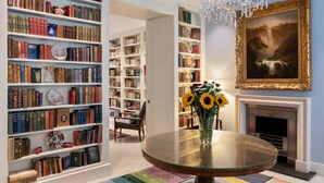 Une pièce avec une table ronde en verre, des étagères à livres, une cheminée et un lustre.