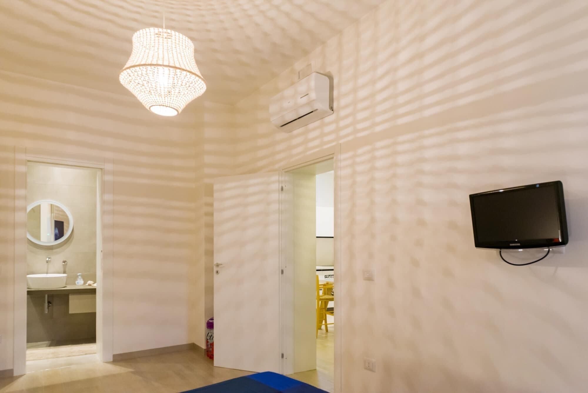 A modern room with a large mirror, a flat-screen TV, a ceiling fan, and a door leading to another room.