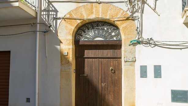 A stone archway with a wooden door, a metal gate, and two electrical boxes on the wall. - LA NASSA SUITES MAZARA (Mazara del Vallo)
