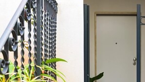 A door with a small peephole, a metal gate with a chain, and a plant in the foreground. - LA NASSA SUITES MAZARA (Mazara del Vallo)