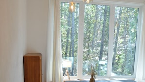 Een eetgedeelte met een houten tafel, twee zwarte stoelen, een vaas en een uitzicht op een bos door het raam.