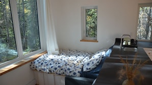 Een gezellige kamer met een ingebouwde bank langs het raam, een klein tafeltje met een vaas, en uitzicht op het bos.