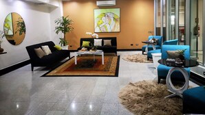 A modern living room with a black sofa, a coffee table, and blue armchairs. There is a painting on the wall and a potted plant.