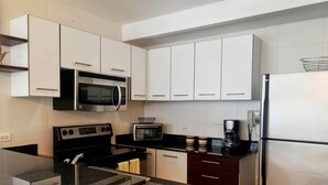 A modern kitchen with white cabinets, a black stove, a microwave, a toaster, and a refrigerator.