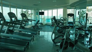 A gym with treadmills, elliptical machines, and stationary bikes, large windows with a city view.