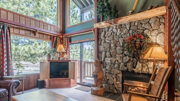 Un salón acogedor con chimenea de piedra, una estatua de oso y un amplio ventanal con vistas a árboles.