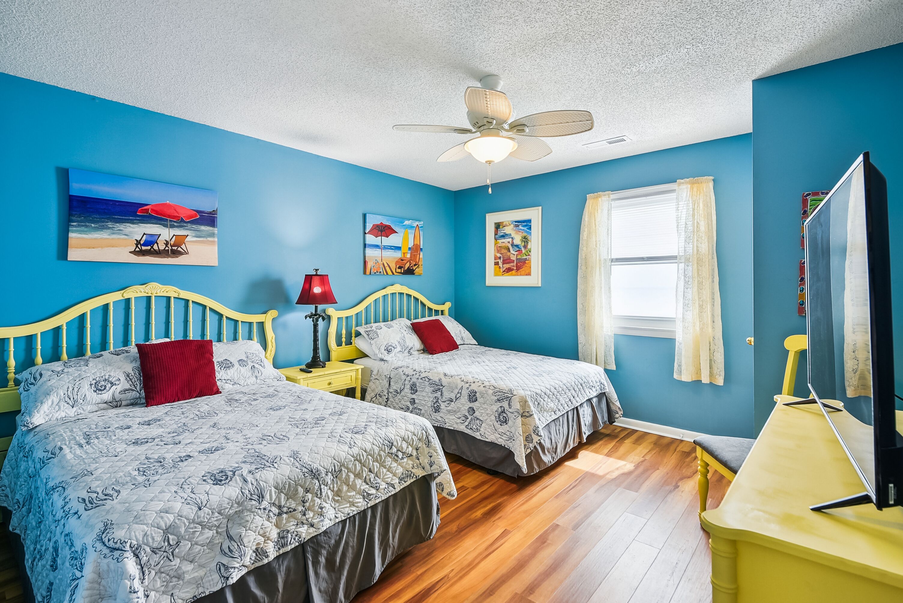 A bedroom with two beds, a ceiling fan, and artwork on the walls.