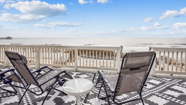 A balcony with two lounge chairs and a small table, overlooking a beach with a pier in the distance. - Pet Friendly Ocean Front Home - Shore Delight (North Myrtle Beach)