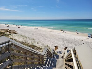 Ein Strand mit hölzernen Stegen, die zum Ufer führen, klarem türkisblauem Wasser und einigen entspannten Personen im Sand.