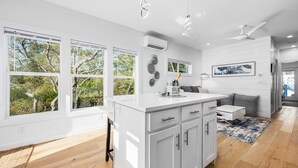 Een moderne keuken met witte kasten, een centraal eiland en grote ramen met uitzicht op groen.